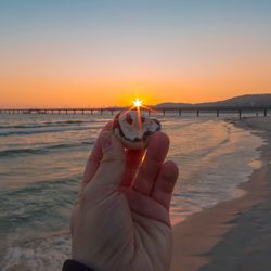 Close-up of hand holding sea during sunset