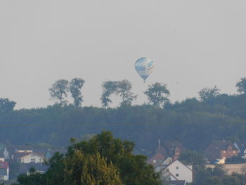 Hot air balloon flying over trees and buildings against sky