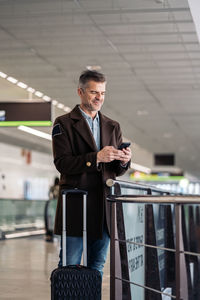 Man holding smart phone while standing near railing