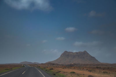 Road leading towards mountains against sky