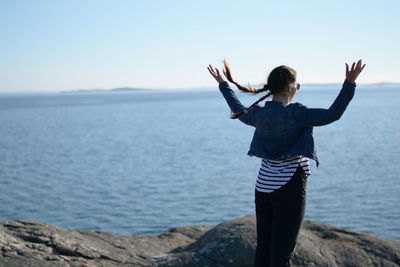 Rear view of woman with arms outstretched looking at sea against sky