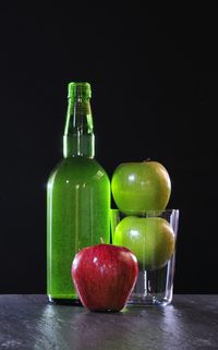 Fruits in glass bottle on table against black background