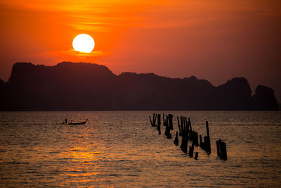 Silhouette wooden posts in sea against sky during sunset