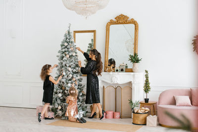 Mom and daughters decorate the christmas tree for the new year celebration