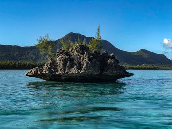 Rock formation in sea against clear blue sky