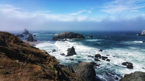 Scenic view of rugged coastline and sea against foggy windy sky