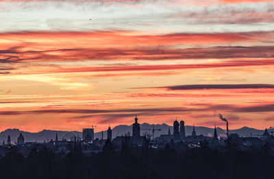 Silhouette buildings against cloudy sky during sunset