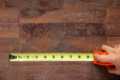 Cropped hand of woman holding measuring tape on wooden table