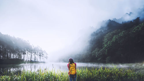 Rear view of woman standing by lake against sky