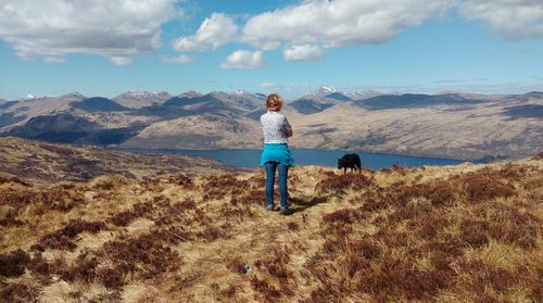 Rear view of woman with dog against mountain and sky