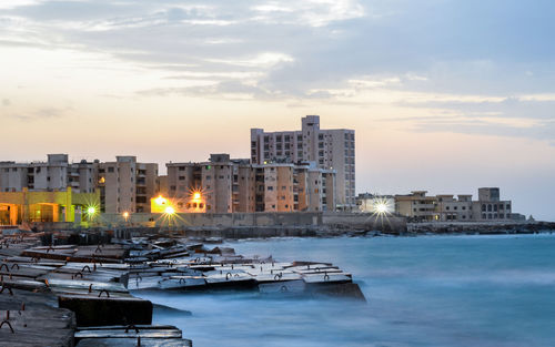 Buildings by sea against sky during sunset