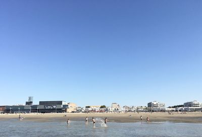 View of people on beach against clear blue sky