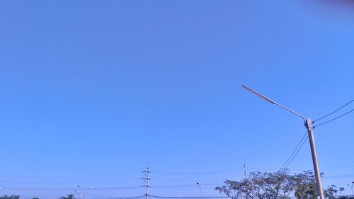 Low angle view of electricity pylon against clear blue sky