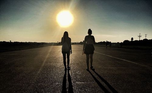 Rear view of silhouette men walking on road against sky