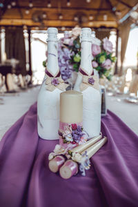 Candles and champagne bottles decorated with white, pink and purple artificial flowers, ribbons