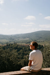 Side view of woman sitting on mountain against sky