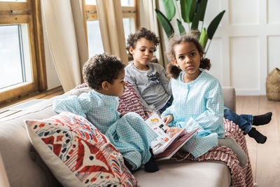 Siblings with book on sofa at home