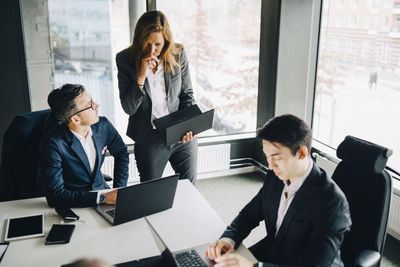 Businesswoman discussing with colleague over laptop while businessman working at conference table in office