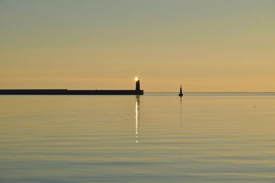 Silhouette lighthouse in sea against sky during sunset