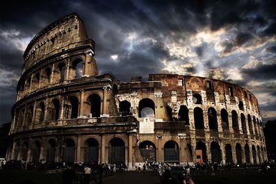 People at historic coliseum against cloudy sky