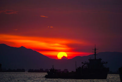 Silhouette sailboats in sea against orange sky