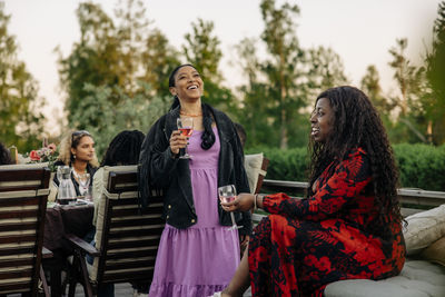 Young female friends enjoying drinks while talking to each other at dinner party