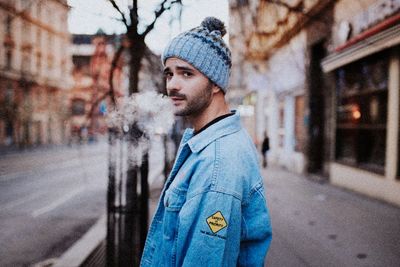 Portrait of young man looking away while standing on street in city