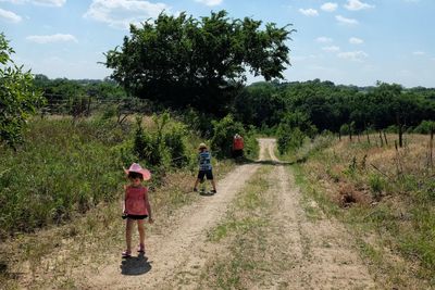 Children playing on dirt road amidst field during sunny day