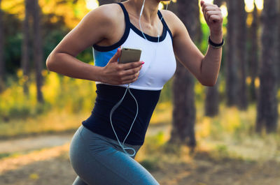 Midsection of woman running with smart phone