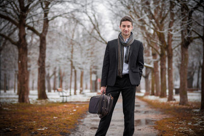 Portrait of businessman standing against bare trees during winter
