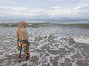 Rear view of woman standing in sea against sky