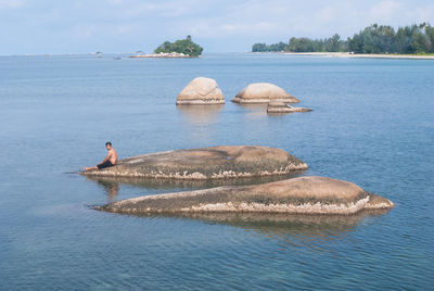 Man sitting on rock on sea against sky