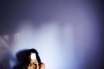 Shirtless woman using phone by white wall