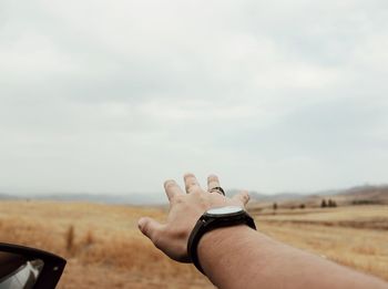 Cropped hand of man gesturing on field against cloudy sky