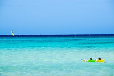 People floating in sea against clear sky tropical beach vacation