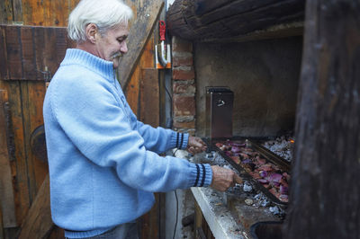 Senior man checking meat grilled on barbecue grill