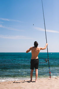 Rear view of shirtless man standing at beach against sky