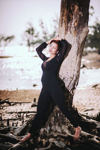 Portrait of woman standing by tree trunk