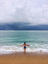 Rear view of woman with arms outstretched while standing at beach