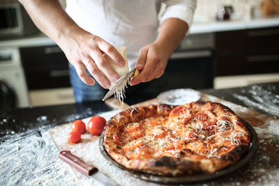 Male hands rubbed cheese grated on pizza, pizza cooking in a real home interior lifestyle 