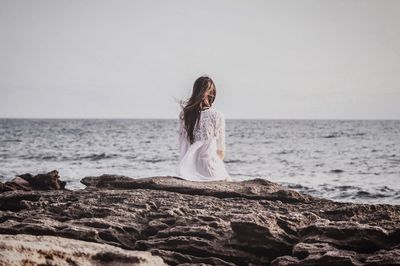 Young woman on rock by sea against sky