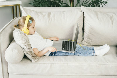 Little girl 4 years old in yellow headphones in front of a laptop.