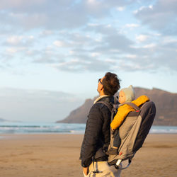 Rear view of woman standing at beach against sky