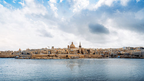 View of buildings by river against cloudy sky