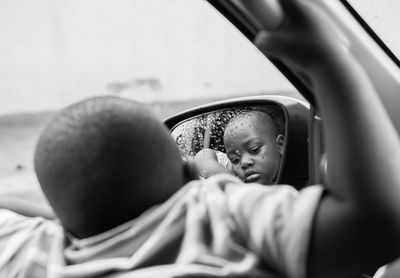 Close-up of boy with reflection on side-view mirror