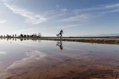 Cheerful young woman riding bicycle sky on sunny day at ebro's delta, spain