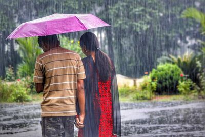 Rear view of women walking on wet umbrella during rainy season