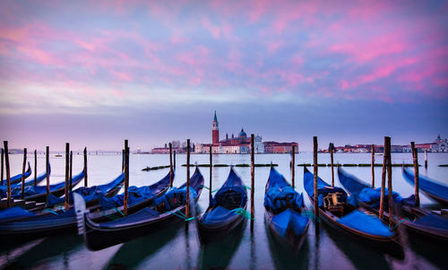 Gondolas moored on canal against cloudy sky during sunrise
