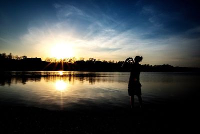 Silhouette man standing by lake against sky during sunset