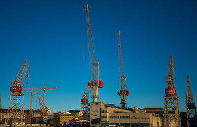 Low angle view of cranes against clear blue sky